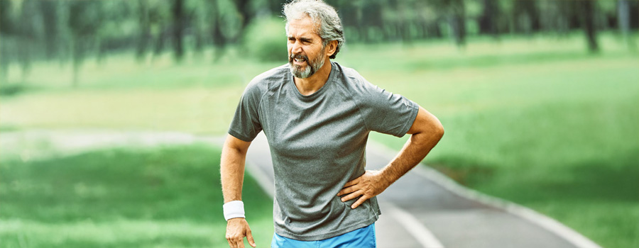 Elderly man on outdoor running track, holding his hip in pain