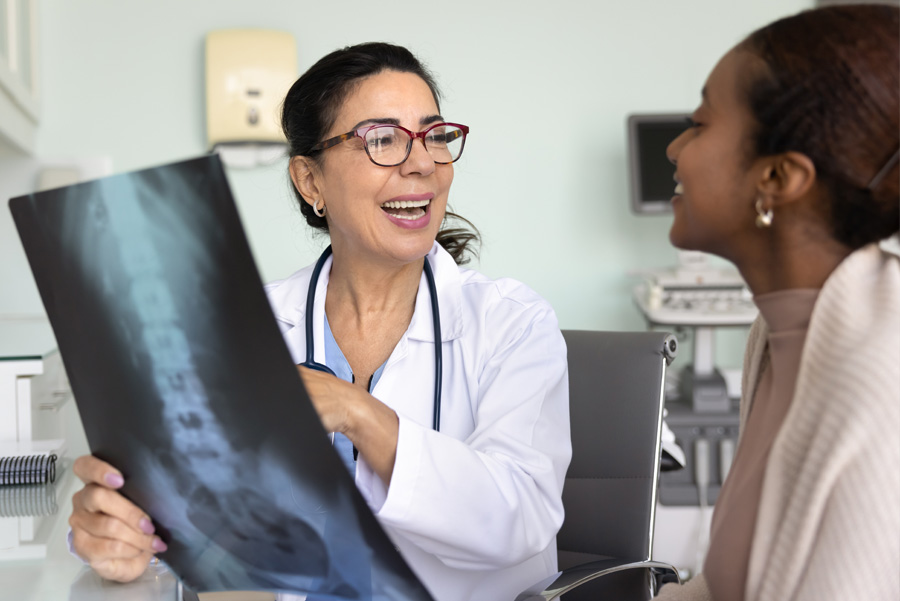 Smiling female doctor showing female patient X-ray of her spine at UTMB Health clinic