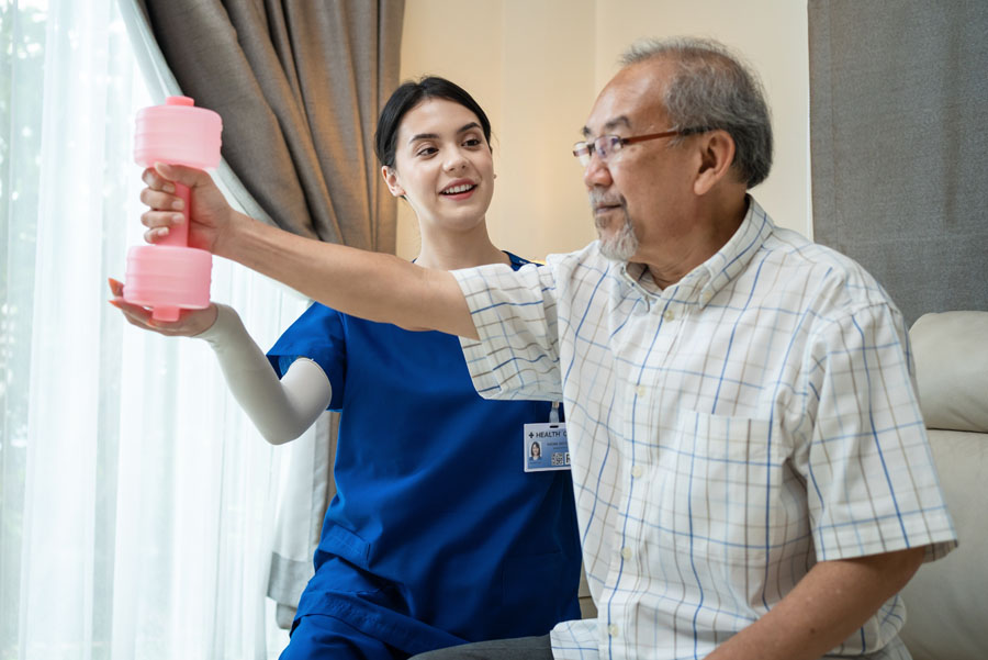 Female therapist at UTMB Health helping elderly man to exercise by using dumbbell. 