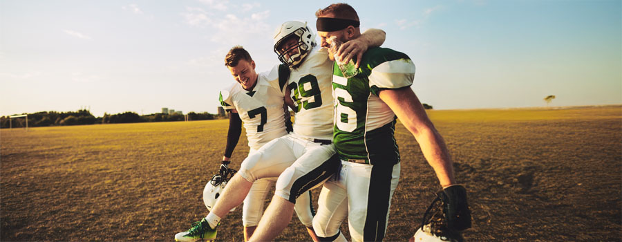Two football players carrying an injured football player off the field after an injury.
