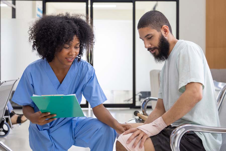 Female nurse with clip board examining seated male patient with wrapped knee for tendinitis knee injury.