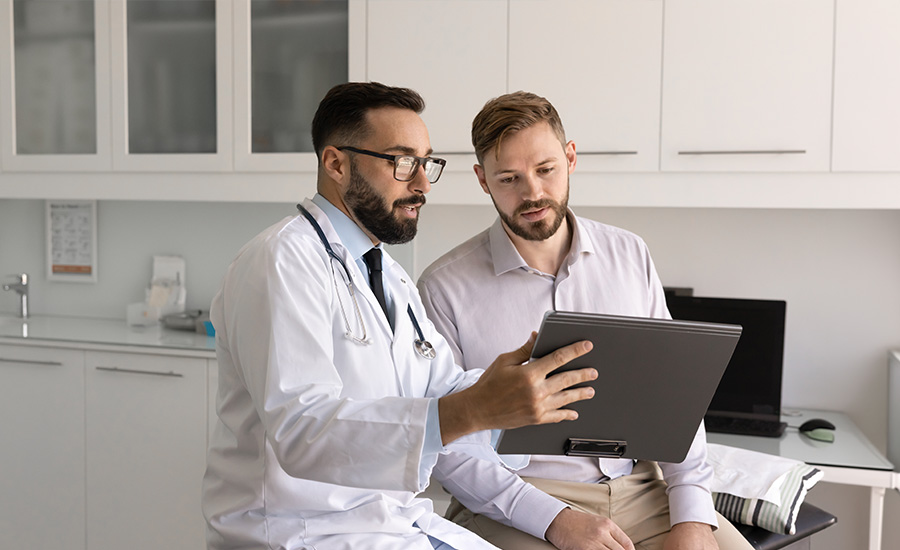 Male doctor showing male patient something on tablet in clinic setting