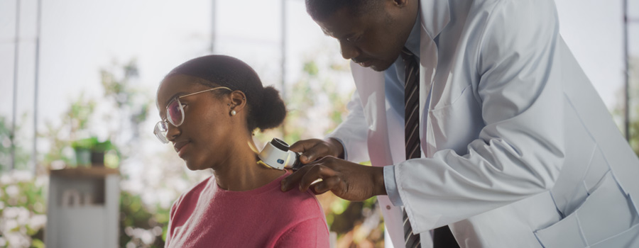 Male doctor using a dermatoscope to examine the neck of a female patient