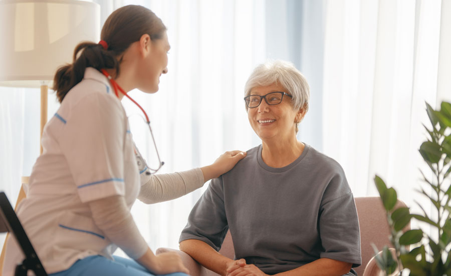 Seated female doctor placing comforting hand on shoulder of seated smiling, elderly female patient
