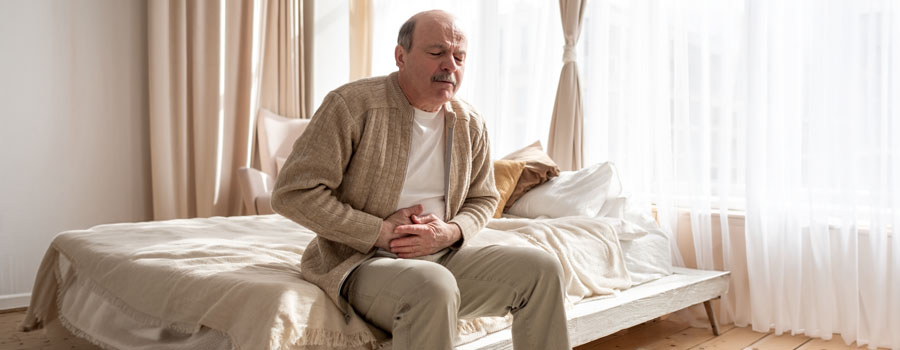 Man in pain, seated on his bed while touching his stomach