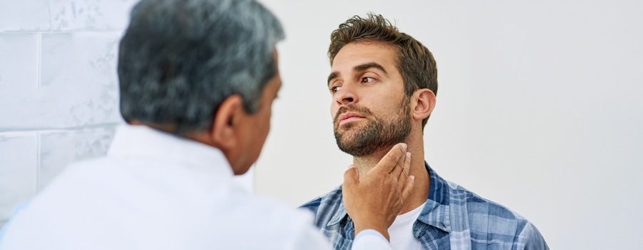Male doctor examining the thyroid gland of a male patient at a clinic