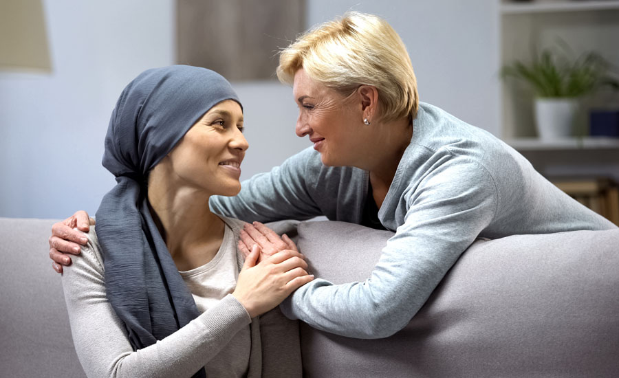 Smiling woman placing her arm around the shoulder of a smiling woman wearing a head wrap