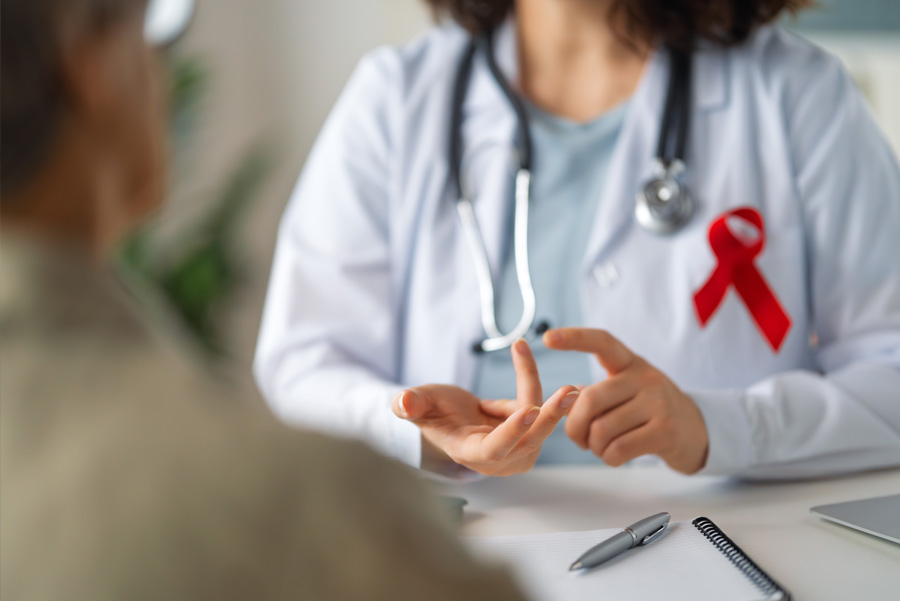 A UTMB health care provider wearing a white coat and red ribbon speaks to a patient during a medical visit.