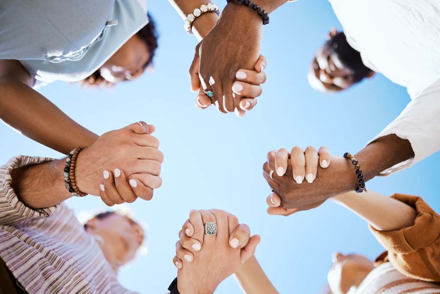 A group of diverse individuals holding hands in a circle, viewed from below, showing unity and support.