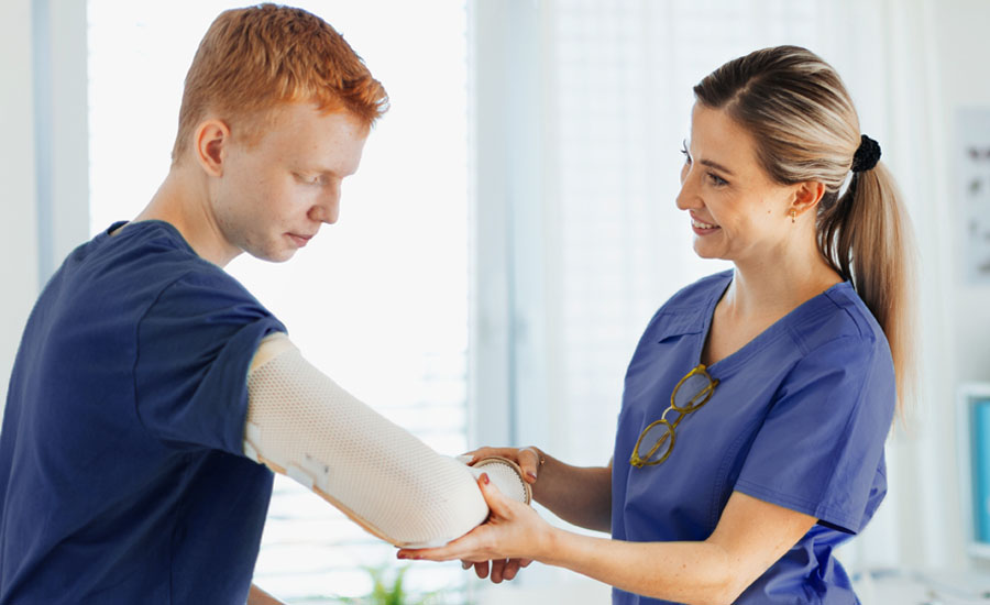 Female doctor placing brace on young man’s arm for fractured elbow
