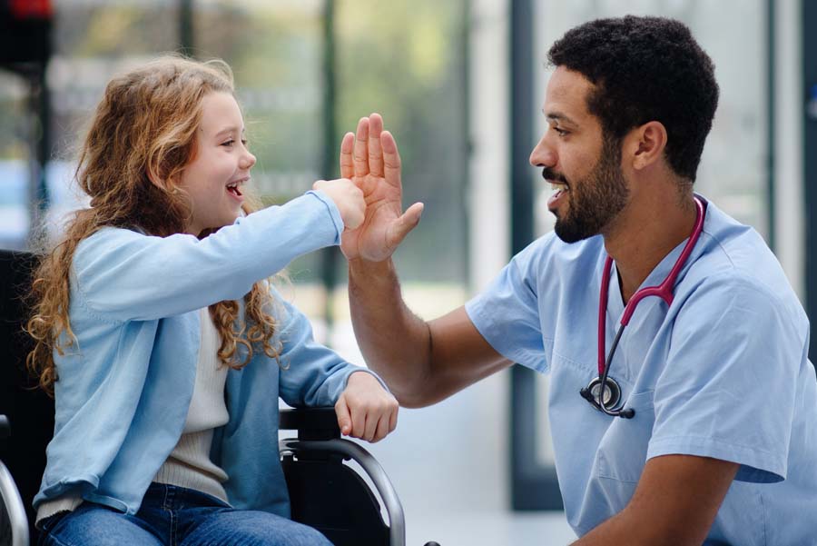 Male doctor giving a high five to a girl in a wheelchair