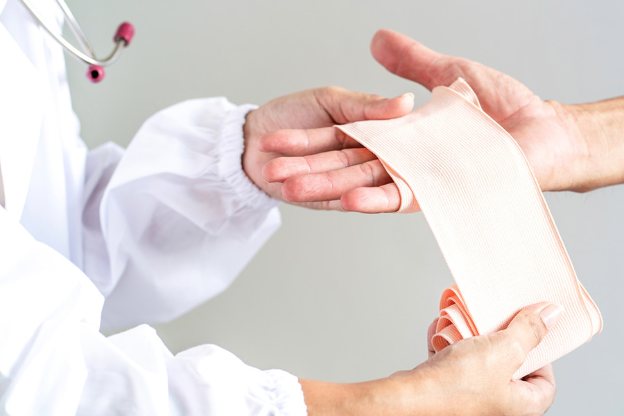 Closeup of person getting their injured hand wrapped with gauze by a medical professional