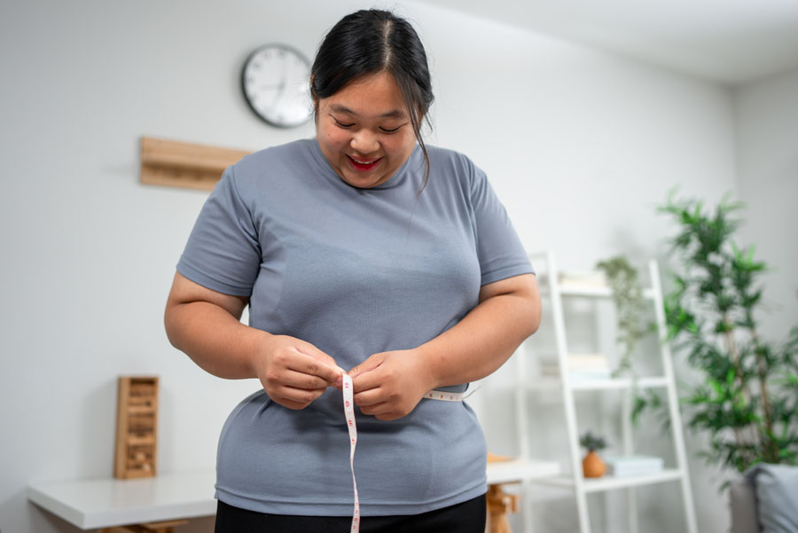 Happy, curvy woman measuring her waistline after weight loss surgery