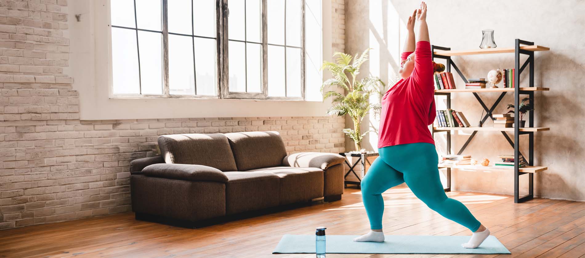 Curvy woman doing yoga stretches on mat indoors 