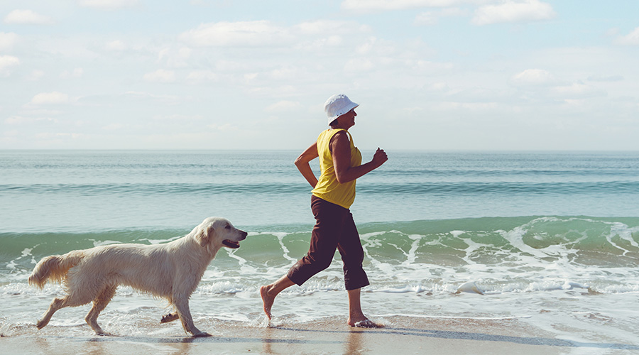 A woman walks her dog along the shoreline, representing active living after menopause.