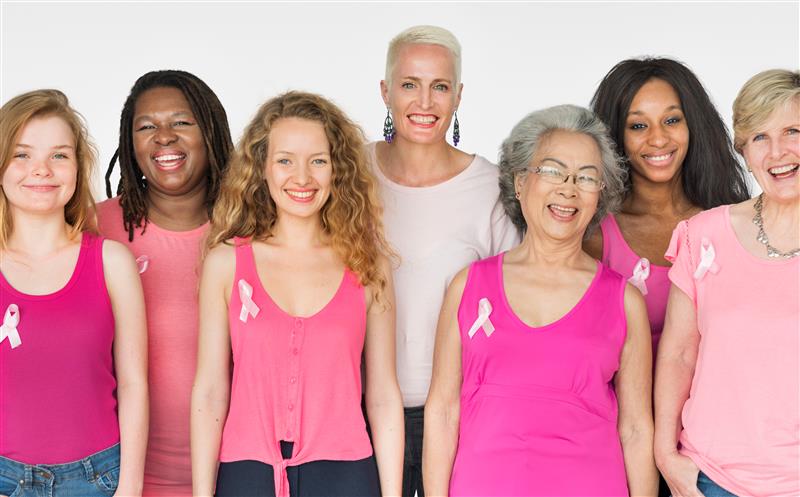 A group of people wearing pink tops and pink breast cancer awareness ribbons stand together against a light background
