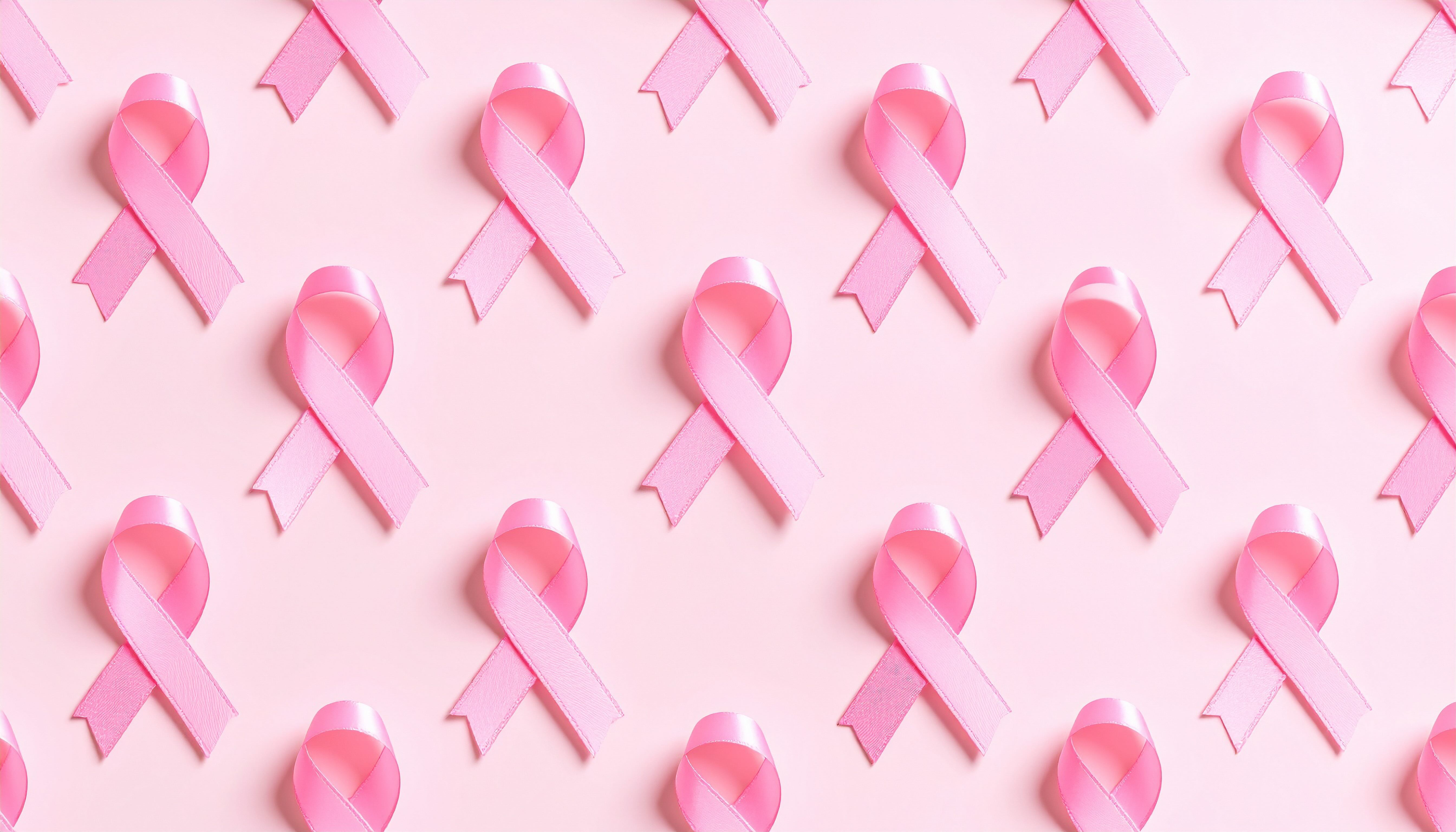 Pink breast cancer awareness ribbons arranged in a repeating pattern against a soft pink background