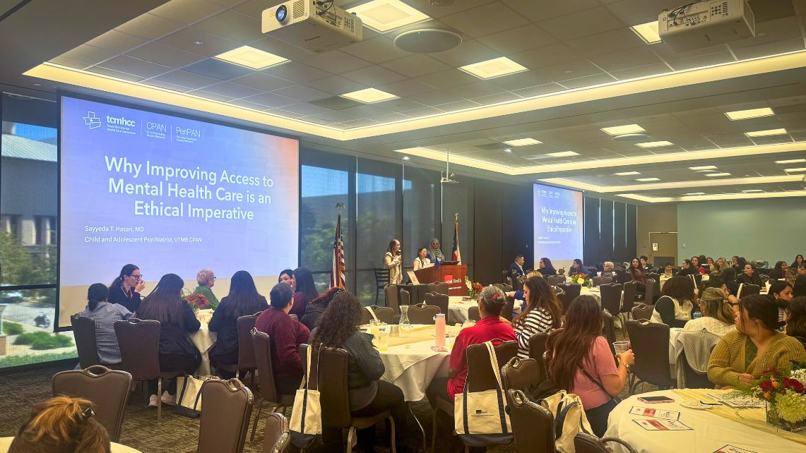 Audience seated at round tables in a conference room during the 3rd Annual Howard and Lillian Becker Perinatal Care Conference at UTMB, with presenters speaking at a podium and large screens displaying a presentation on mental health access