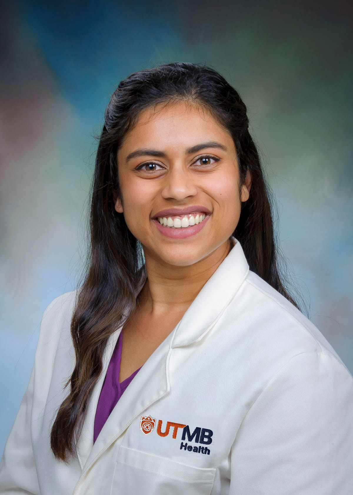 Portrait of a person wearing a white UTMB Health lab coat, facing the camera against a blue-green studio background.