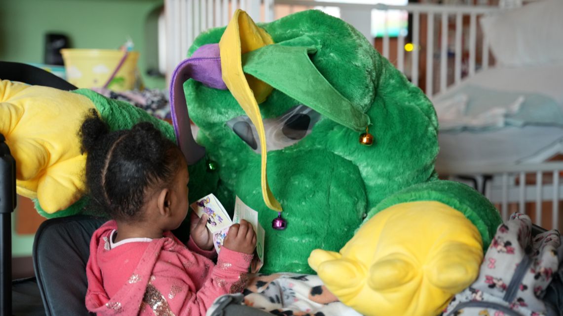 Pediatric Hospital Teacher Sheryl Bucsanyi dressed in a Mardi Gras alligator costume interacts with a small child