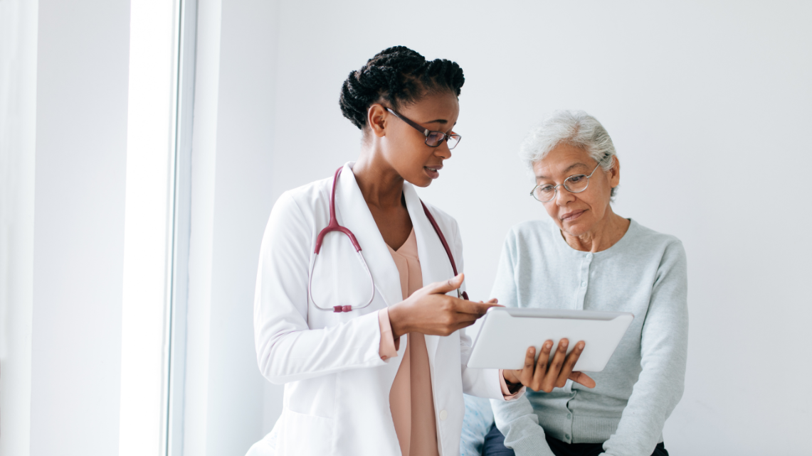 A doctor in a white coat and with a red stethescope speaks to a patient.