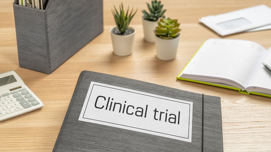 a picture of a desk with calculator, notebook, pants and a folder that has a sign on it that reads clinical trial