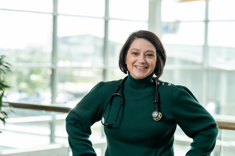 A woman in a green sweater and a stethoscope around her neck smiles for a photo.