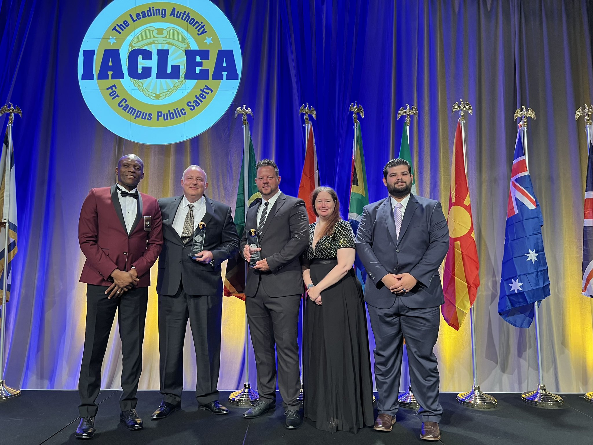 IACLA award presenter with four members of the UTM Police Department standing on stage under round IACLA logo.