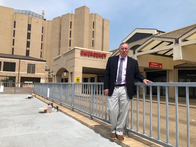 Dr. Dietrich Jehle stands outside the UTMB emergency department entrance, with hospital buildings and “Emergency” signage visible behind him.