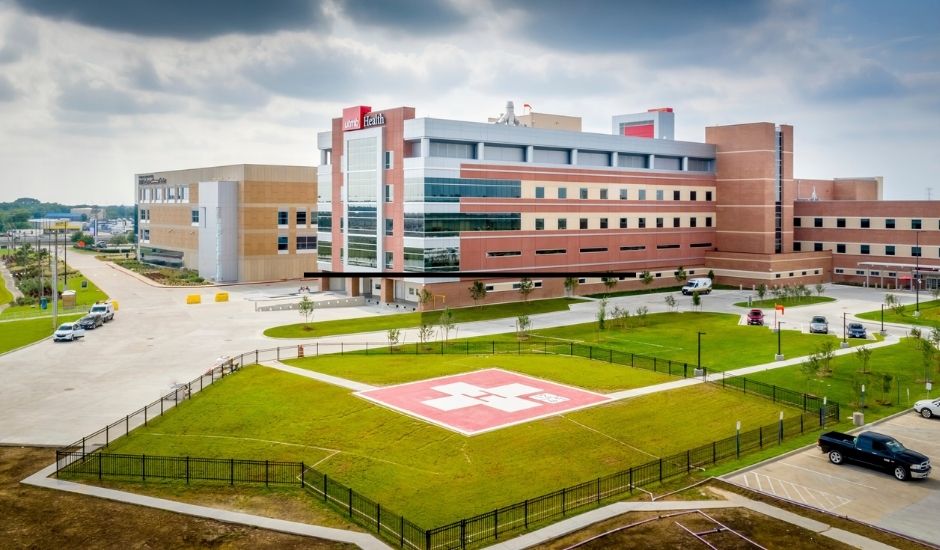 Aerial view of UTMB Health League City Campus hospital, featuring the main medical building and a fenced helipad in the foreground.