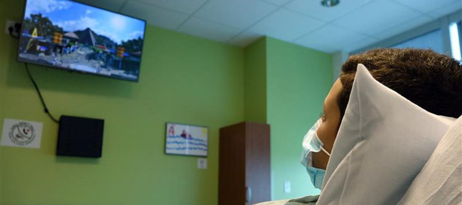A child watches a television screen from a hospital bed.