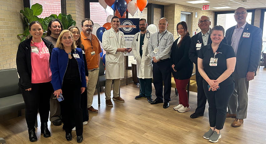 Compassion in Practice 2026 Q1 ambulatory winners: UHC Infectious Disease team, led by Nurse Manager Corey Turner, RN; Medical Director Lucas Blanton, MD; Division Chief Miguel Cabada, MD; and Ambulatory Director Michael Johnson, MBA. Group of UTMB staff gathered indoors during an award presentation, standing near balloons and a sign recognizing team achievement.