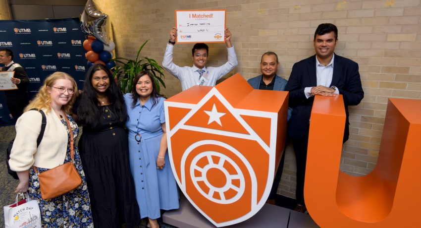 Group of six smiling people pose at a UTMB Match Day celebration, standing beside large orange “UTMB” letters and a shield logo, while one person in the center holds up a “I Matched!” sign, surrounded by balloons and a branded backdrop.
