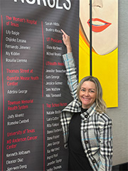 Woman standing in front of a black and red sign pointing to her name.