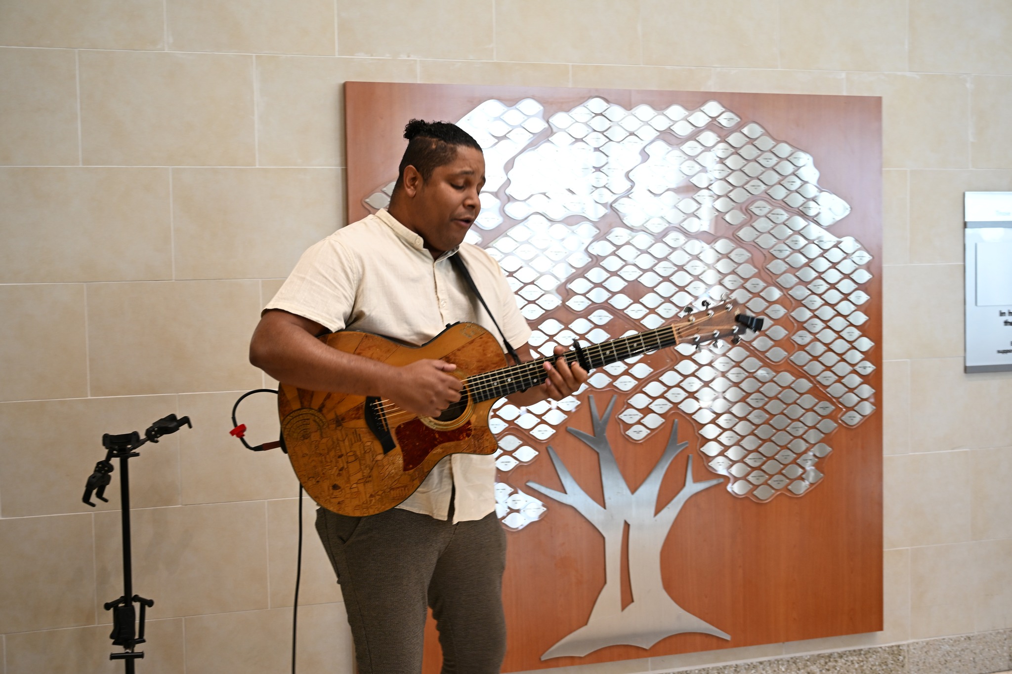 A man plays a guitar in front of an artwork of a tree