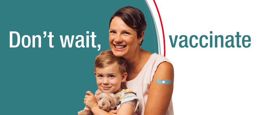 A smiling parent holds a young child wearing a bandage after vaccination, alongside text that reads “Don’t wait, vaccinate,” encouraging childhood immunizations