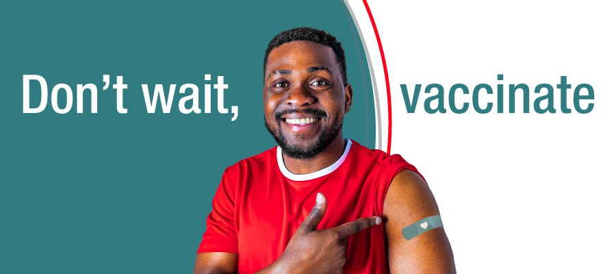 A person pointing to an adhesive bandage on his upper arm against a teal background, with the words “Don’t wait, vaccinate”