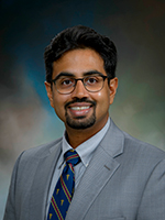 Dr. Raj Vaghjiani, wearing a gray suit and blue, red, and gold tie appears in a headshot.