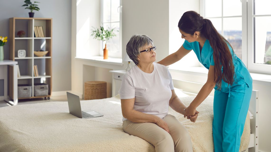 A nurse in blue scrubs checks on an elderly patient