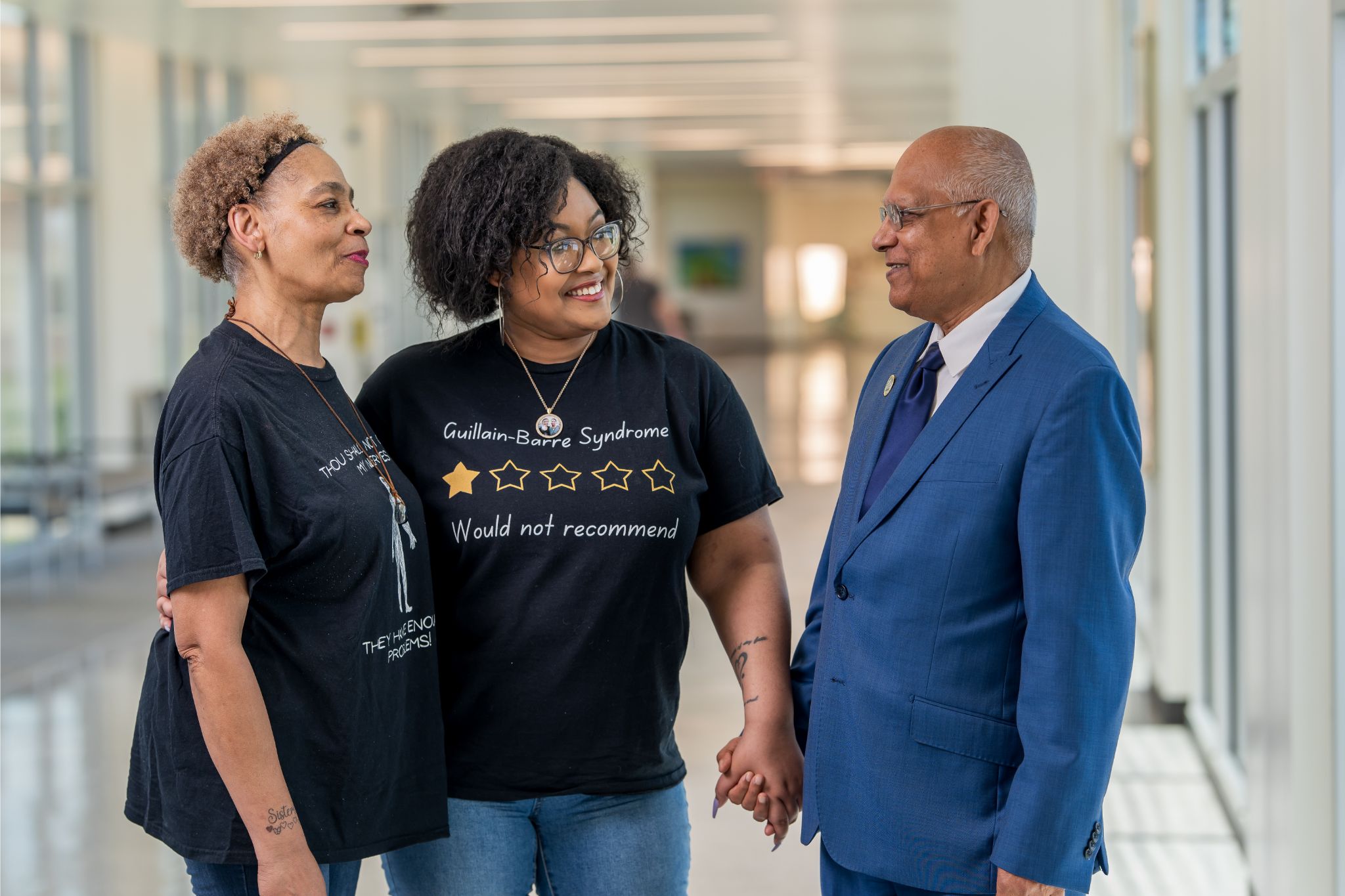 Yuniquie Robinson stands holding hands with her mother, Darlene Robinson, while speaking with UTMB neurologist Dr. Abdul Khan in a hospital corridor, reflecting the care and support that guided her recovery from Guillain‑Barré Syndrome