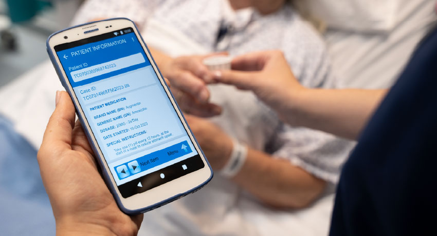 Handheld device displaying patient medication information while a clinician prepares to administer medication at a bedside.