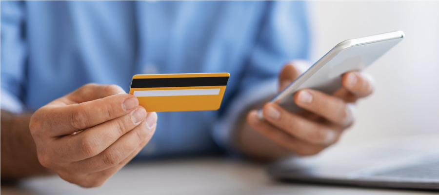 Close-up of a person holding a credit card and using a smartphone, representing electronic payment and managing medical bills