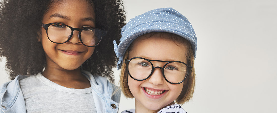 Two young children wearing eyeglasses standing side by side against a light background