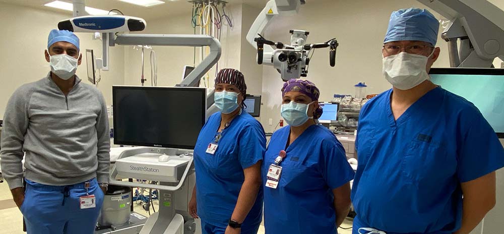 Neurosurgery team standing in an operating room beside advanced surgical monitors and imaging equipment at UTMB Health Clear Lake Campus.
