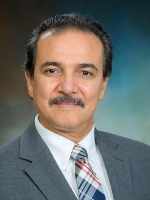Head-and-shoulders shot of a man in a grey suit with dark hair against a studio blue backdrop” 
